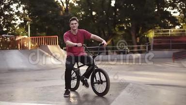 一个年轻人在他的自行车上有一个BMX自行车座椅与坡道，溜冰公园的背景。 BMX骑手的肖像。 街道